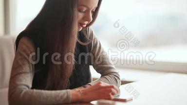 一个年轻漂亮的女孩手里拿着一部手机坐在咖啡馆的桌子旁。 休息一下。